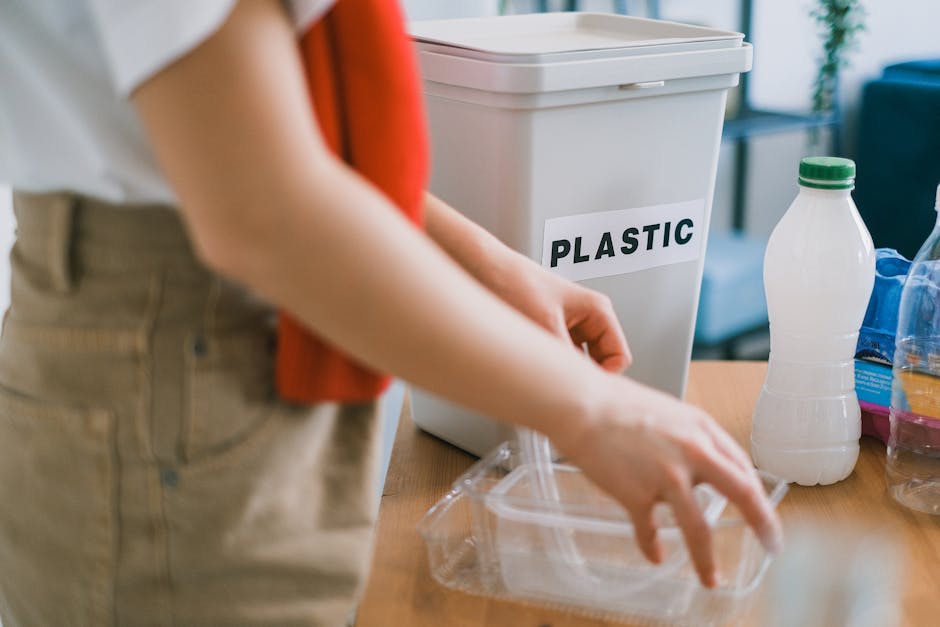 Close-up of a black rubbish bag filled with household waste, tightly knotted at the top, placed inside a property near a neutral-colored wall. The bag appears to be made of plastic and is positioned o