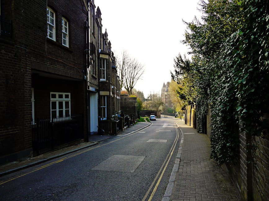 A narrow urban alleyway in Hillingdon, shown in black and white, leading underneath a brick arch bridge with a height clearance sign of 4.2 meters. On the left side, a black van with an open rear door